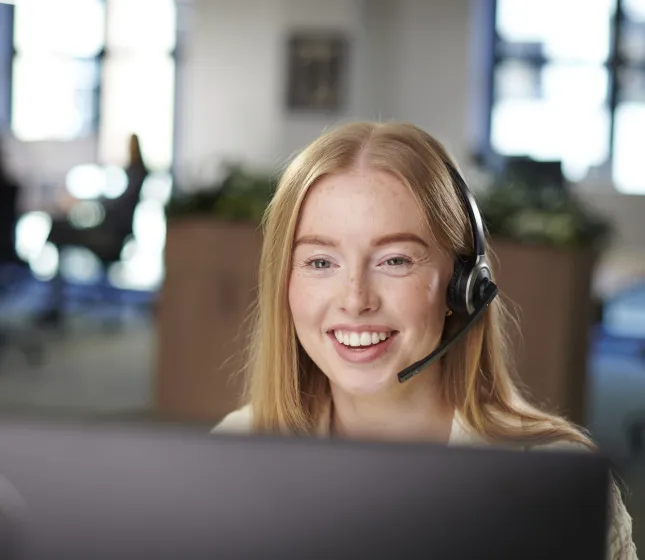 Women looking at a computer monitor wearing a headset and smiling