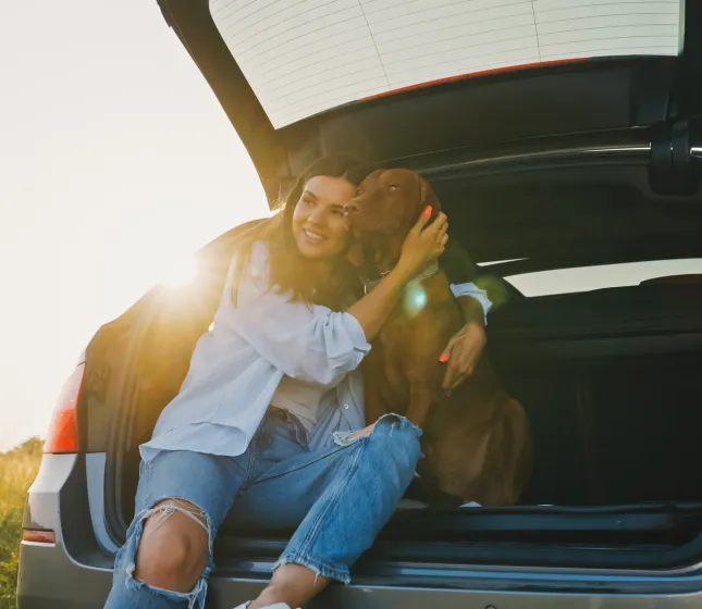 Woman and dog sitting in the back of a car with the trunk open